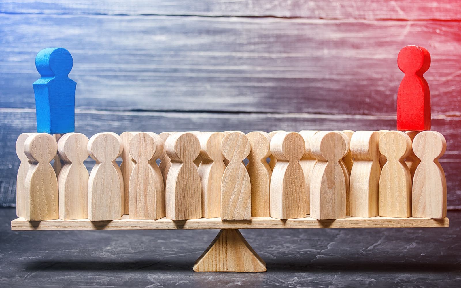 Wooden figures on a level balance scale, one blue figure on the left and one red on the right